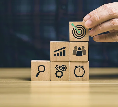 Stacked wooden blocks with icons: target, growth, team, search, gears and clock.