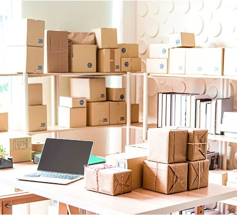 Packing station with stacked cardboard boxes, shelves and a laptop for order fulfillment.